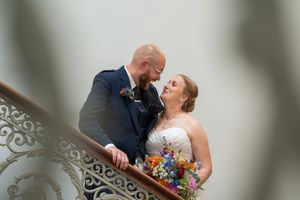 A couple shares an intimate moment on an elegant staircase with ornate architectural details.