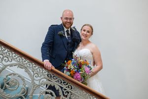A couple poses on a grand staircase with decorative railings and white walls.