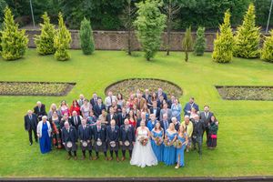 Wedding party and guests gathered on a manicured lawn for a group photo.