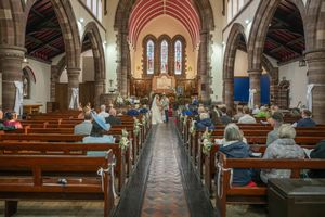 Wedding ceremony inside a traditional brick church with guests seated in wooden pews and couple at the altar.