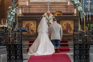 Bride and groom kneeling before a priest at a church altar during a traditional wedding ceremony.