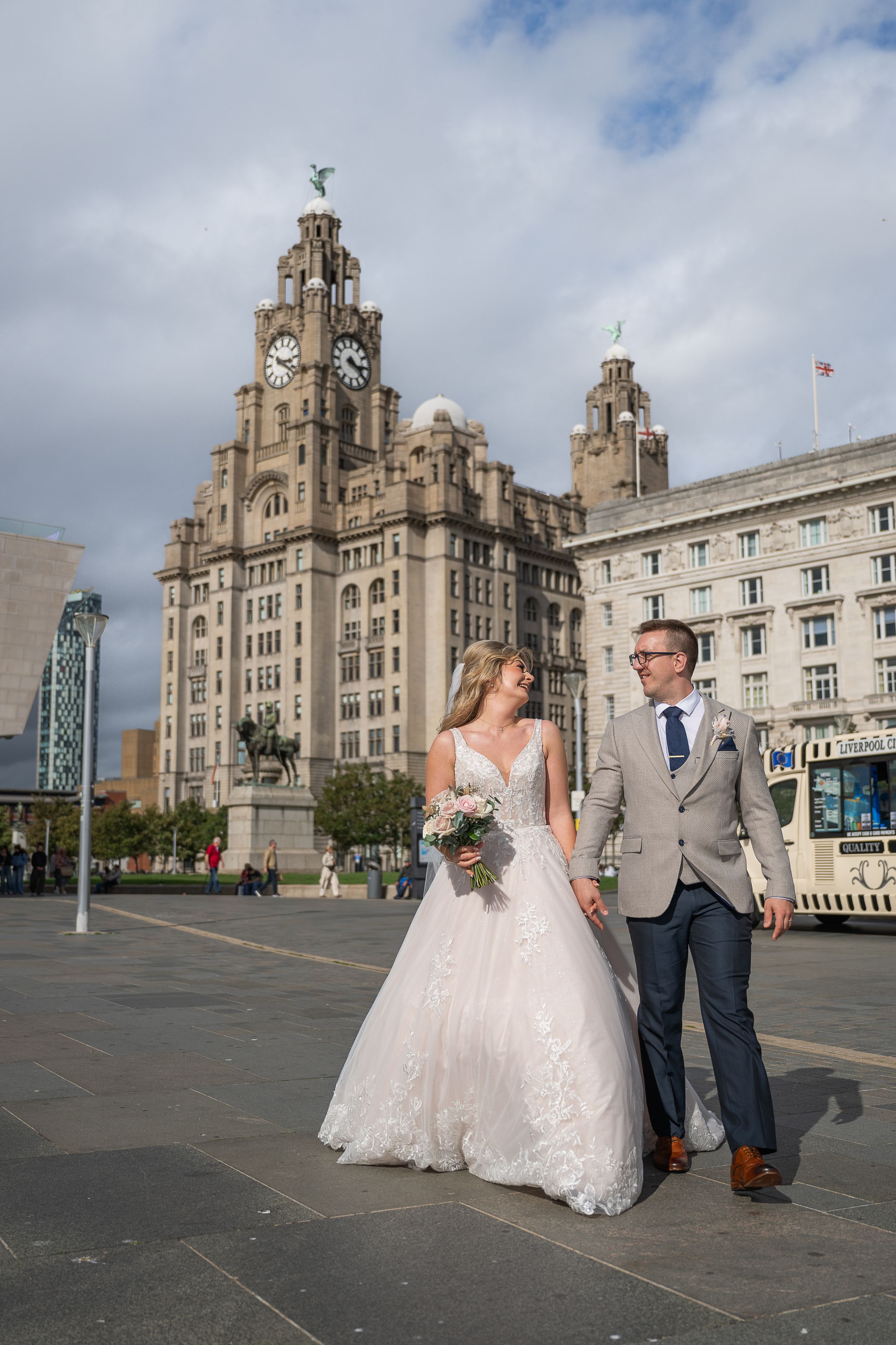 Bride and groom walking hand in hand outside the Royal Liver Building in Liverpool on their wedding day.