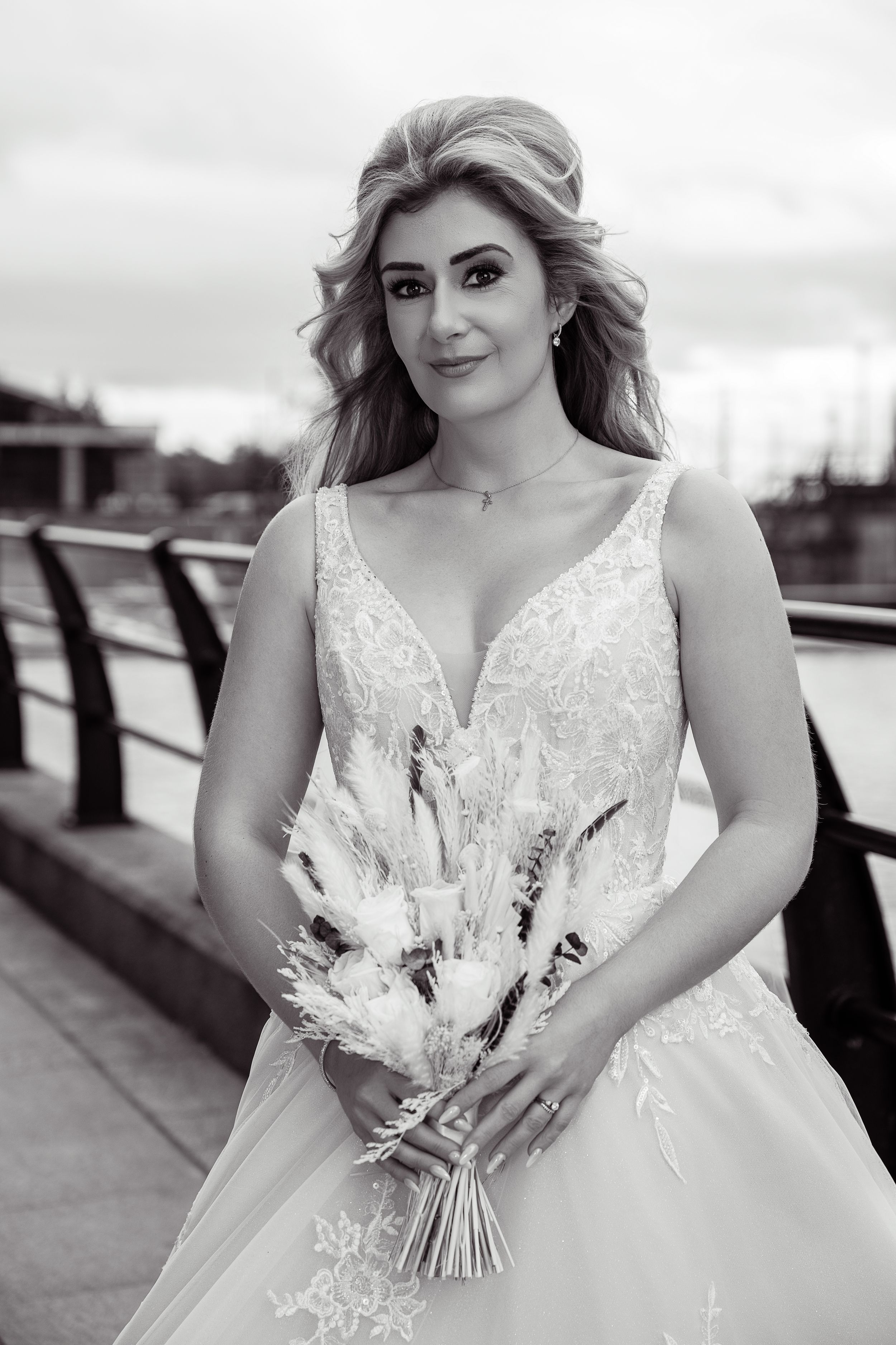 Black and white portrait of a bride in a lace gown holding a dried floral bouquet outdoors.