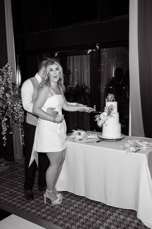 Black and white photo of a bride and groom cutting their wedding cake at an elegant reception venue.
