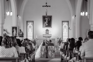 Black and white photo of a wedding ceremony inside a Catholic church with guests seated in pews.