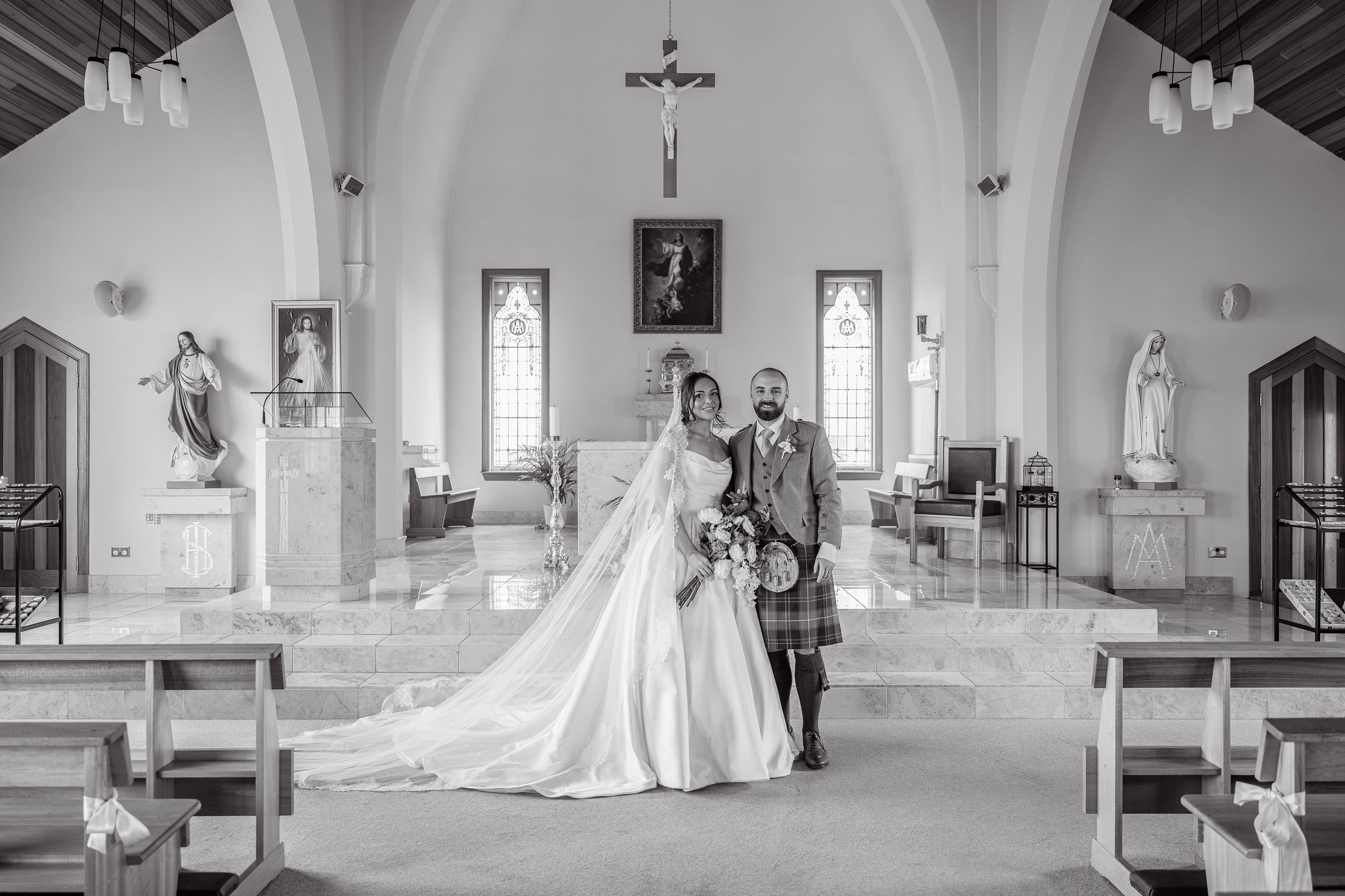 Black and white photo of a bride and groom posing inside a church after their wedding ceremony.