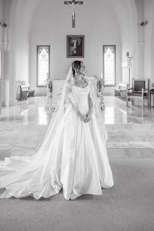 Elegant bride in a flowing white ball gown and veil stands in a sunlit church interior.