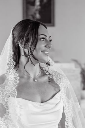 Smiling bride wearing a lace veil and strapless gown with a delicate pendant necklace.