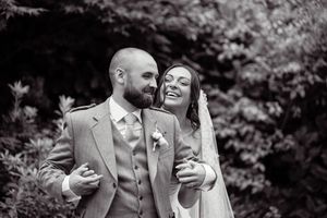 Black and white photo of a laughing bride and bearded groom in a kilt suit, sharing a joyful moment outdoors.