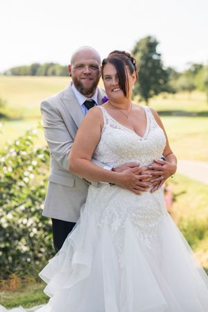 Romantic couple embracing in a sunny field with white dress flowing.