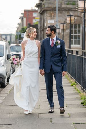 Newlyweds walking hand in hand along an urban pathway.