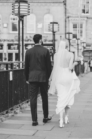 A couple walking along a street with lampposts in black and white.
