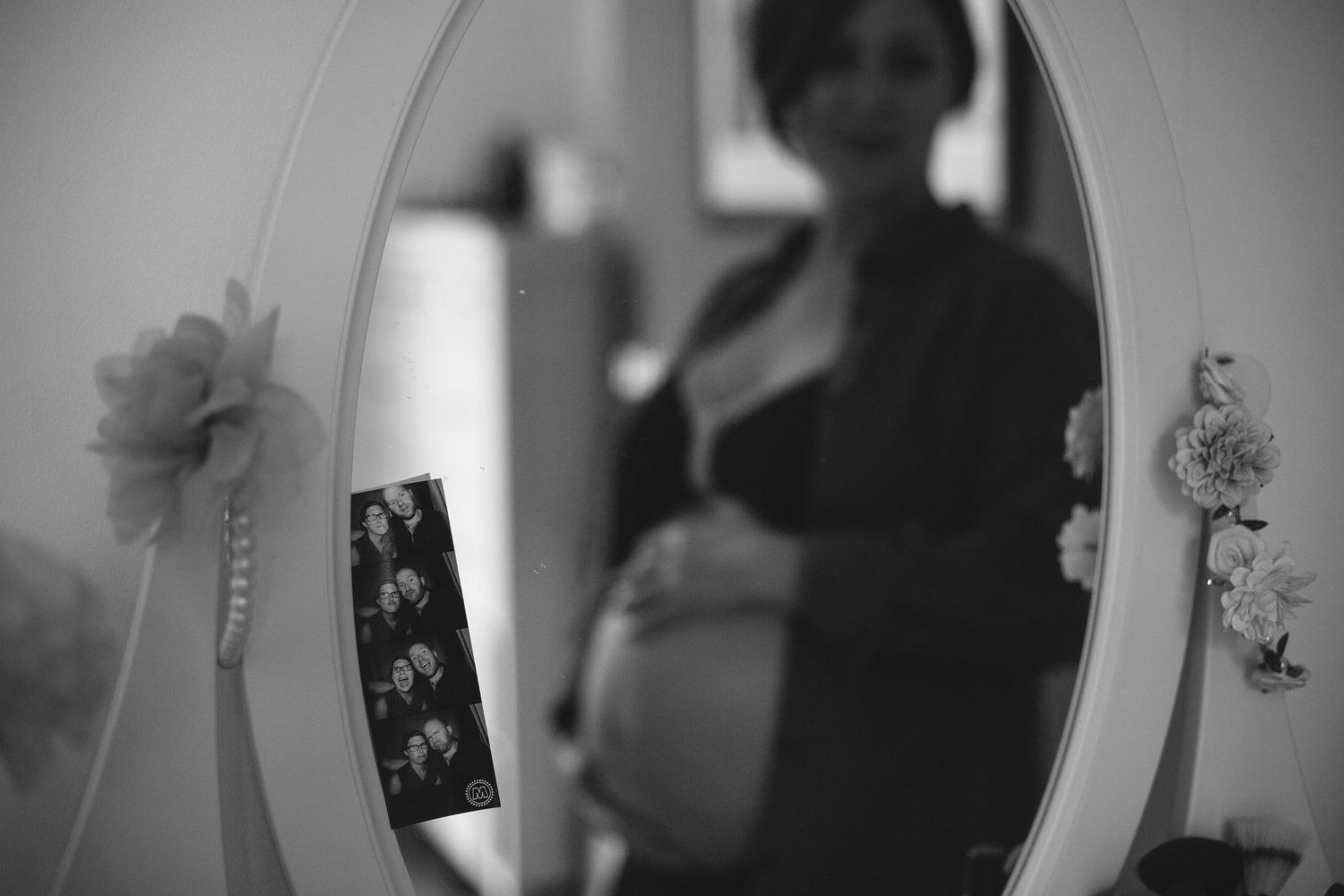 A black and white silhouette reflection shows a pregnant figure in a mirror with flowers decorating the frame.