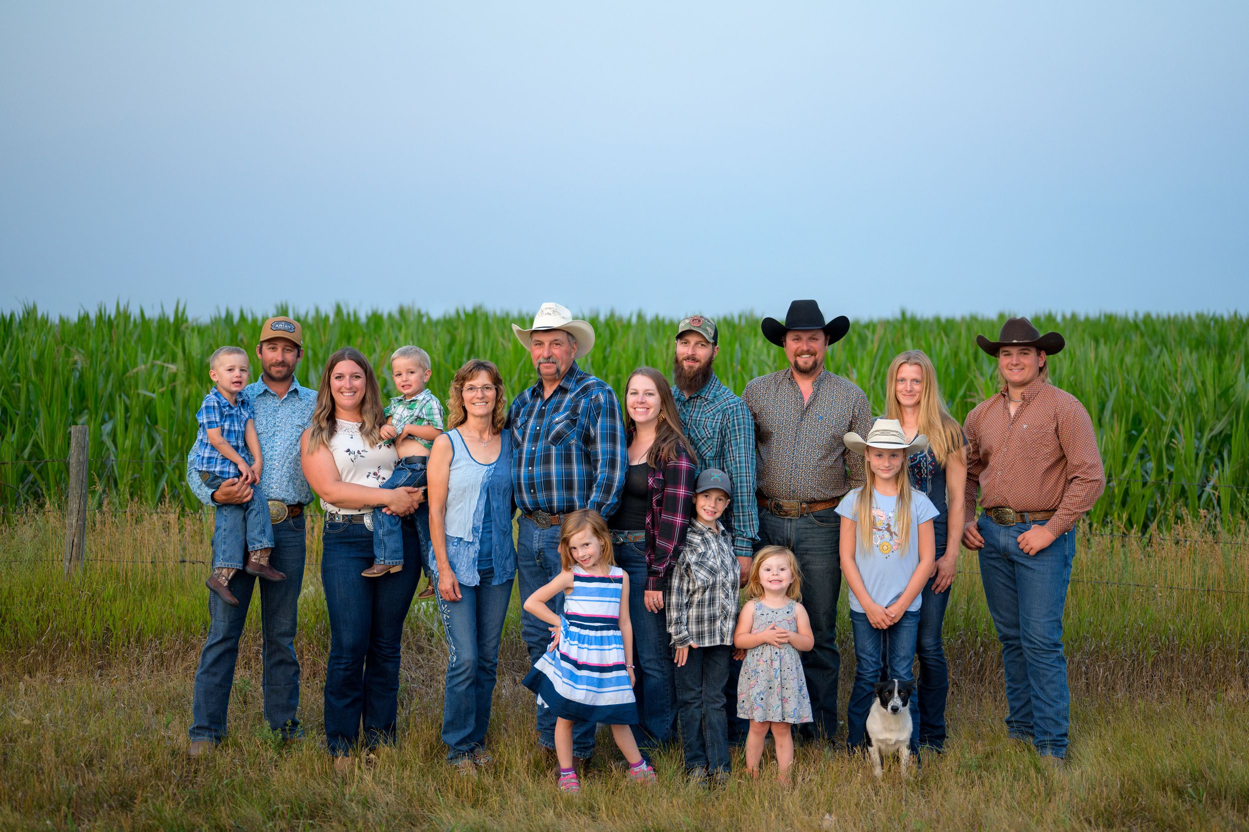A group of people in western attire stand together in front of a green field at dusk.