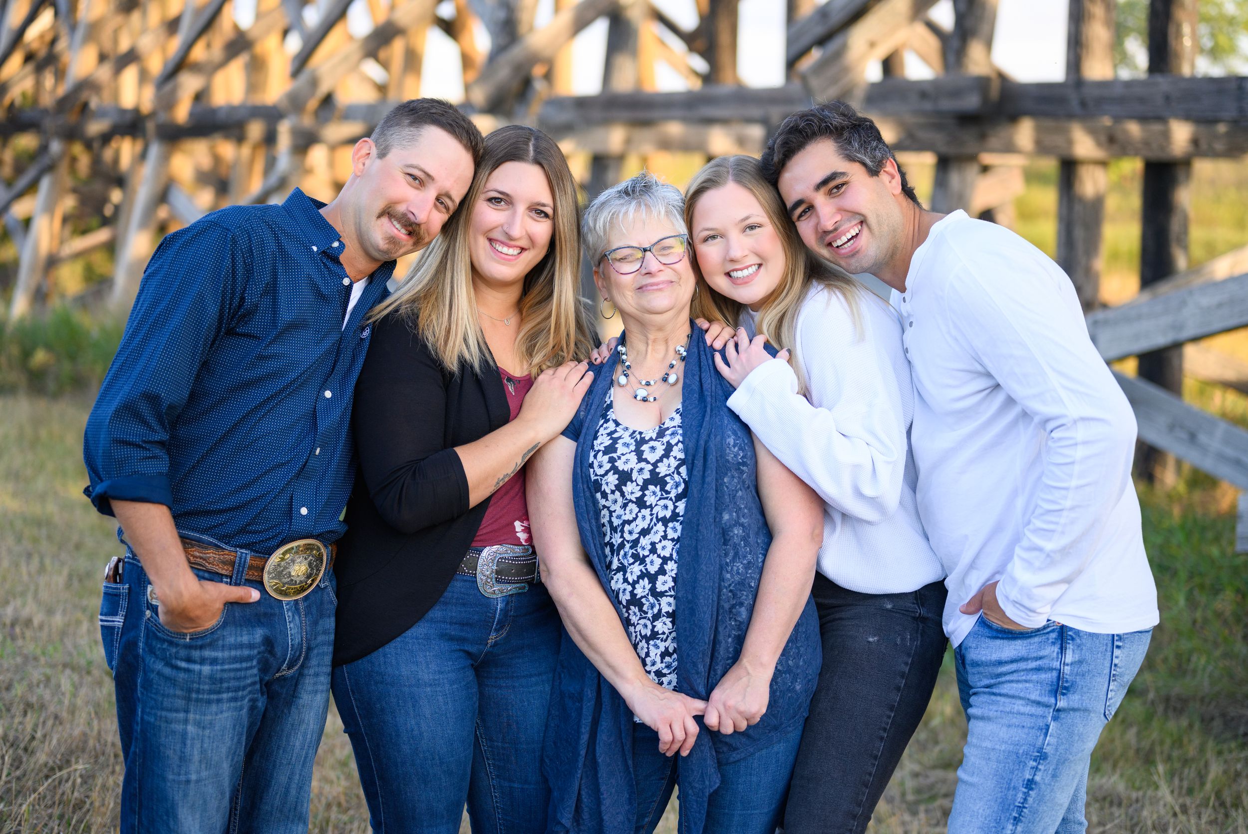 A group of people smiling together outdoors against a wooden fence during golden hour lighting.