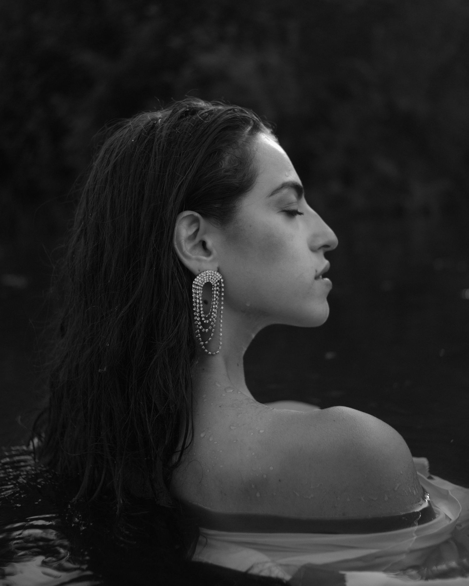 Ritratto artistico in bianco e nero di una donna con i capelli lunghi e orecchini in acqua.
