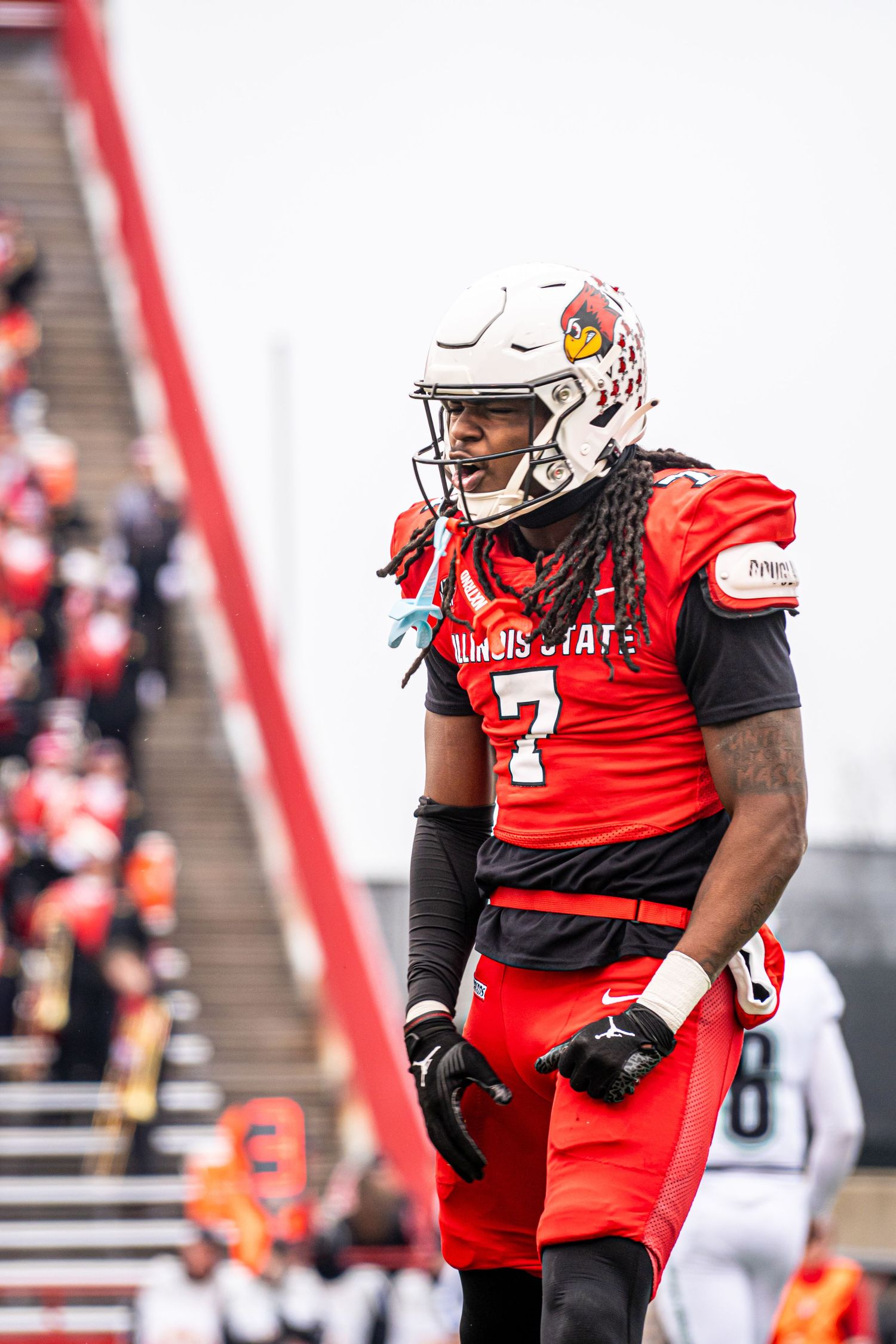 Louisville Cardinals football player in red uniform and white helmet stands on field during game.