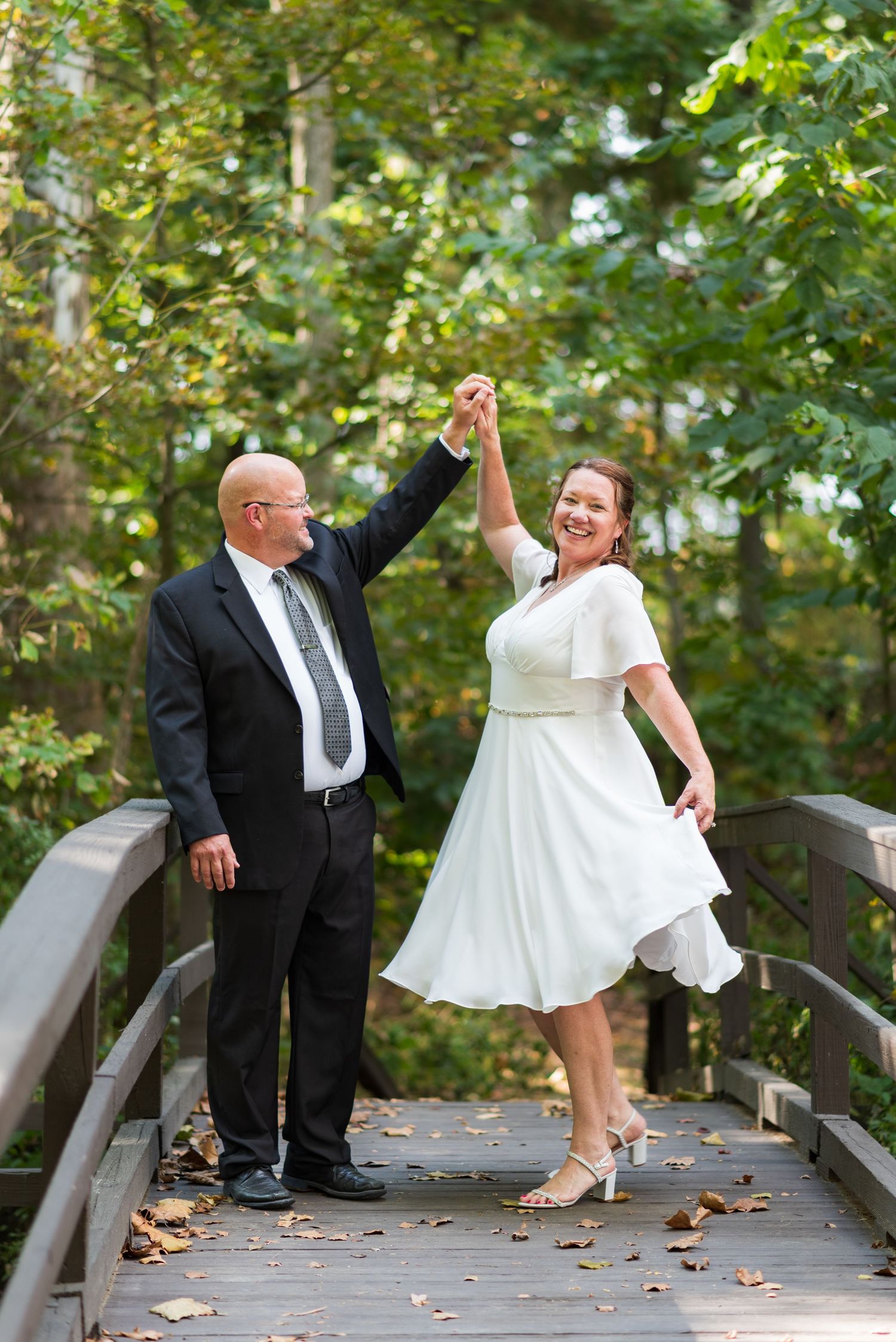 Couple dances playfully on wooden bridge surrounded by autumn foliage.
