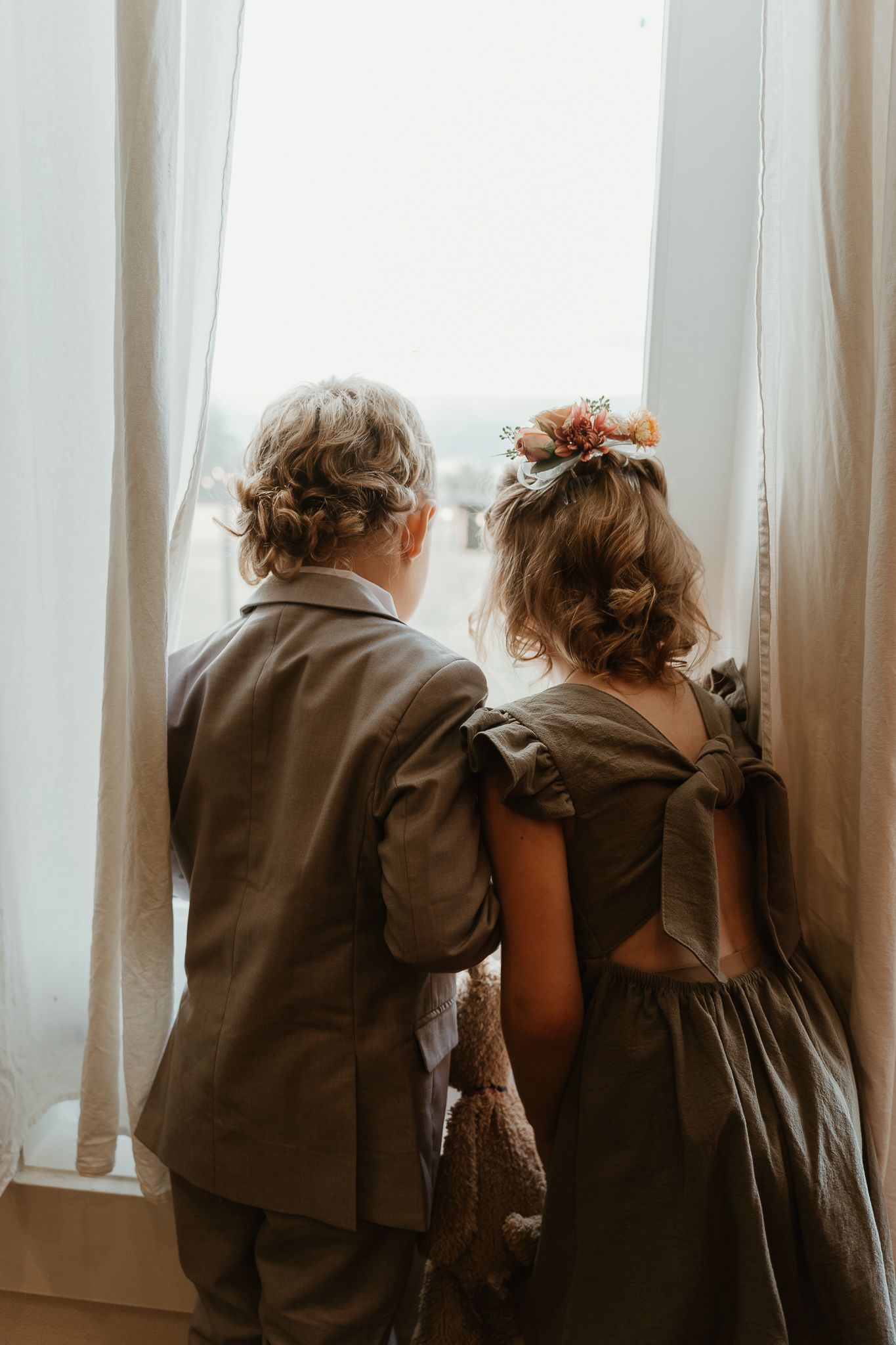 Flower girl and ring barrier looking out window to see wedding guest arrive.