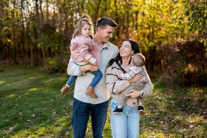 Happy family with two young children posing outdoors in autumn foliage park setting.