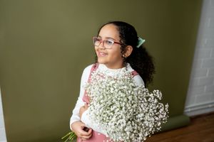 Smiling girl with glasses holding large bouquet of white baby's breath flowers indoors.