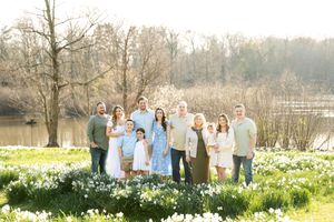 A large extended family poses together in a field of white daffodils near a peaceful lake.