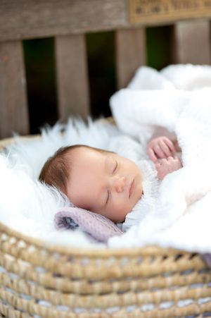 Peaceful newborn baby sleeping in wicker moses basket with white fluffy blanket.