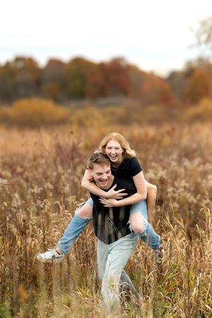 Laughing young woman gets a piggyback ride from her partner through a tall golden grass field.