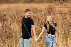Happy young couple holds hands while walking through a golden autumn field, smiling at each other.