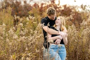 Joyful couple embraces and laughs together surrounded by golden dried wildflowers in an autumn field.