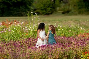 Two girls in dresses hold hands walking through a vibrant wildflower garden.