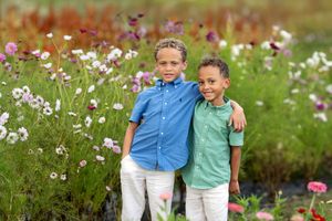 Two smiling brothers pose together in a colorful wildflower field on a sunny day.