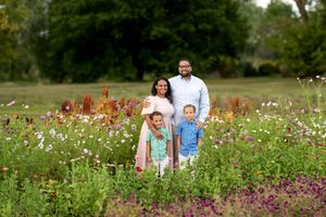A family of four smiles together surrounded by vibrant wildflowers in an open field.