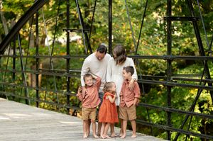 A family of five stands together on a rustic iron bridge surrounded by autumn foliage.