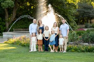 Extended family with children posing on lawn in front of decorative garden fountain.
