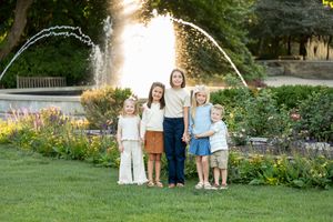 Six children posing together on a green lawn with a decorative garden fountain behind them.