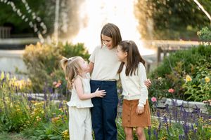 Three sisters sharing a sweet moment together in a garden with fountain backdrop at sunset.