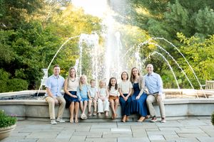 Extended family portrait of adults and children seated by a garden fountain at sunset.