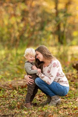 Young mother crouches down to share a joyful moment with her laughing toddler in an autumn park.
