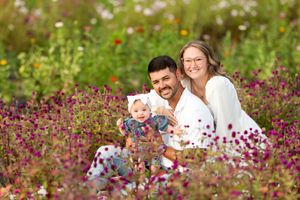 Young family with baby sitting among colorful wildflowers in a vibrant garden field.