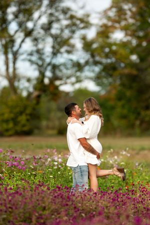 Couple embracing romantically in a blooming wildflower field with trees in background.