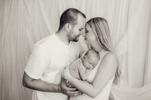 Black and white photo of new parents sharing a romantic moment while holding their sleeping newborn.