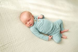 Sleeping newborn baby wrapped in a soft teal outfit on white blanket.
