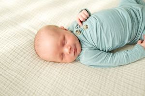 Peaceful newborn baby sleeping in a teal outfit on a white textured blanket.