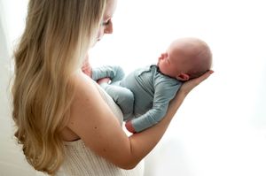 Mother with long blonde hair gently holds her sleeping newborn baby.