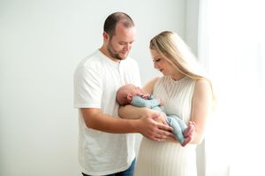 Couple in white outfits lovingly cradles their newborn baby indoors.