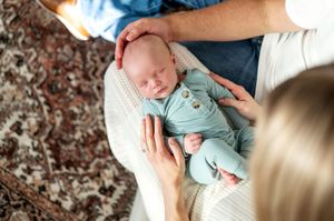 Parents tenderly touch their sleeping newborn baby dressed in teal.