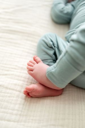 Close-up of tiny newborn baby feet in soft teal pajamas on white blanket.