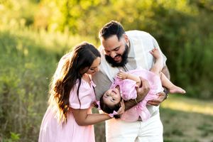 Happy family with father holding laughing baby girl upside down while mother watches outdoors.