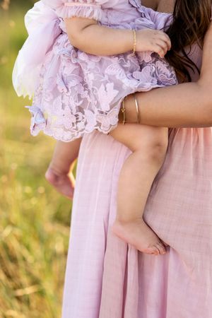 Close-up of a mother in pink dress holding her baby girl in a delicate lavender lace dress outdoors.